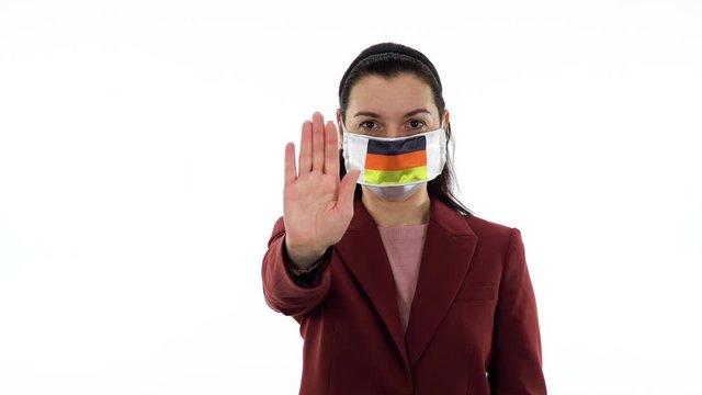 Virus and disease prevention concept. Pandemic and quarantine. Woman wears a protective medical mask with the image of the flag of Germany. Woman shows stop gesture meaning someone to stop right now.