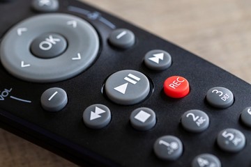 A close up portrait of a remote control to operate a surround sound system, television or other electronic device. The focus is on the play/pause, stop, record and fast forward and rewind buttons.
