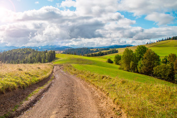 old clay road on top of mountains. Beautiful rural scenery with trees and fields on hills. Tourist route. Outdoor recreation.