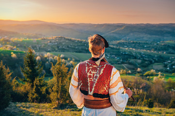 Young man in folk costume standing in spring nature at sunrise. Edit space.