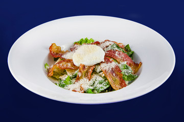 Salad with fragrant breadcrumbs, bacon, parmesan and fresh leaves lettuce, dressed with soft cheese. Closeup on a white plate on a blue background.