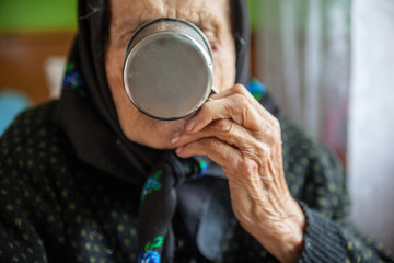 Fototapeta na wymiar Old woman drinking out of the metal mug.
