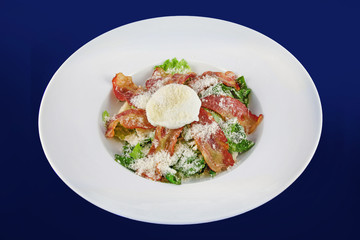 Salad with fragrant breadcrumbs, bacon, parmesan and fresh leaves lettuce, dressed with soft cheese. Top view on a white plate on a blue background.