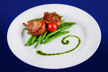 Fried pork medallions on skewers with string beans and one whole tomato. Flat lay top view on a white plate on a blue background. Ketogenic diet - high-fat nutrition. Paleo Diet. Pegan diet.
