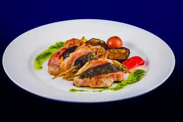 Turkey medallions stuffed with herbs on skewers with grilled vegetables and pesto sauce on a white plate on a blue background.