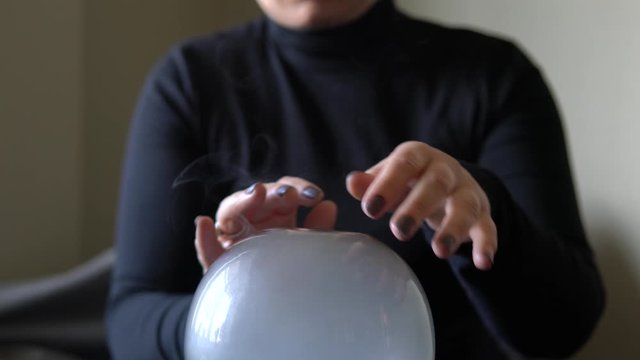 Fortune teller holding hands above magic crystal ball with smoke around. Conceptual footage of practicing black magic and occultism.