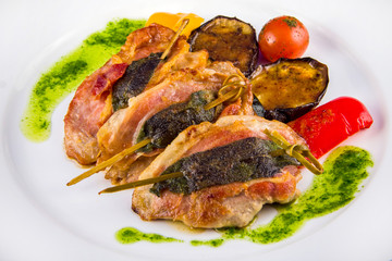Turkey medallions stuffed with herbs on skewers with grilled vegetables and pesto sauce, closeup on a white plate.