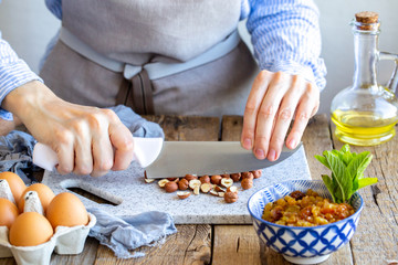 Grinds hazelnuts. A cook grinds a nut on a board with a knife. Hazelnuts on the board. stuffing with cinnamon, nuts and raisins for strudel. Cook at home. Ingredients for the pie.
