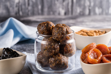 Energy balls of dried fruits and nuts in a glass jar, next to the ingredients for cooking-dried apricots, prunes, almonds.