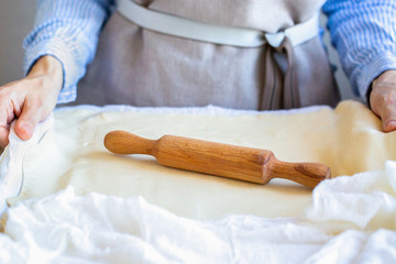 Obraz na płótnie Canvas The rolling pin is on the test. The girl rolls the dough with her hands. Cooking pasta. Work with puff pastry at home 