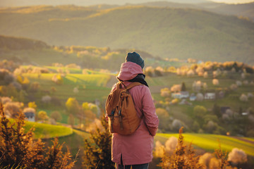 Young woman with vintage backpack standing in beautiful spring nature, warm sunrise light and...