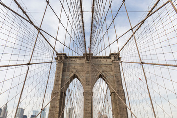 Brooklyn Bridge, photo from inside the bridge, perspective of one of the arches with the cables creating geometric shapes in the sky, in the middle you can see the US flag, photographs of New York
