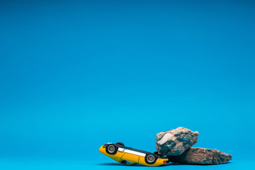 Yellow, sport car sitting turned over underneath a boulder, on blue background.