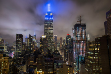 empire state building illuminated with a blue light at night, illuminated Manhattan buildings viewed from a rooftop