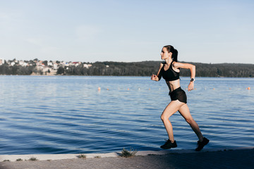 Photo of an athletic girl dressed in black during a morning jog on a city beach in the morning.