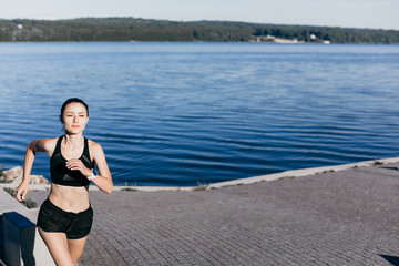 Photo of an athletic girl dressed in black during a morning jog on a city beach in the morning.