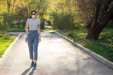 Woman wearing medical mask, alone walks in the park during Covid 19 outbreak. Protection in prevention for coronavirus. Social Distancing concept.