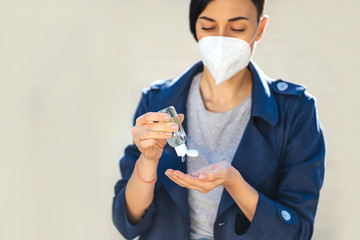 Woman wearing medical mask, using small portable antibacterial hand sanitizer on the street during Covid 19 outbreak. Protection in prevention for coronavirus.