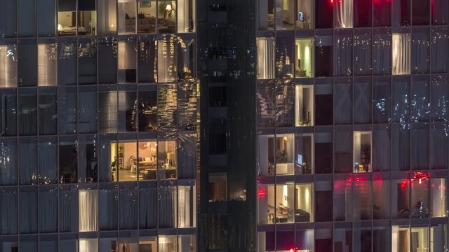 Night view of office and apartment building timelapse. High rise skyscraper with blinking windows with people moving inside. Aerial view from above. Pan down