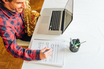 man making notes on sheet music while taking his saxophone online course