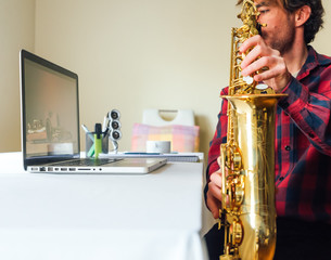 man looking at the laptop and playing while watching his saxophone online course