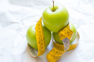 Closeup fresh green apples fruits with measuring tape isolated on white background. Slim diet and eating for healthy.