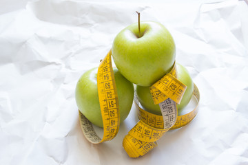 Closeup fresh green apples fruits with measuring tape isolated on white background. Slim diet and eating for healthy.
