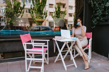 A beautiful young caucasian businesswoman drinking coffee and working on a laptop in a cafe