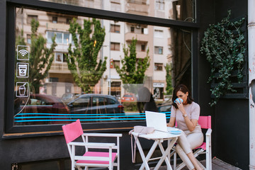 A beautiful young caucasian businesswoman drinking coffee and working on a laptop in a cafe