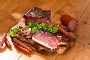 Smoked ham and sausages with parsley and basil on the wooden table.