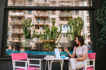Beautiful young caucasian woman with phone and laptop in cafe