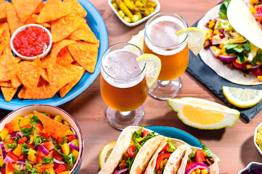 Table With Tacos, Mango Salsa, Nachos With Sauce, Guacamole, Lemon Beer For Cinco De Mayo Celebration Party. Appetizers And Traditional Mexican Dishes For Family Dinner On Wooden Table Top, Copy Space