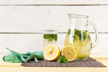 Lemonade with lemon and mint in a jug on a yellow rustic table.