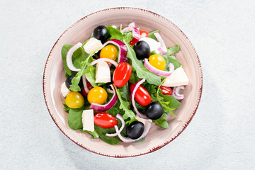 Greek salad closeup on concrete background. Top view of vegetable salad with feta cheese, arugula, cherry tomatoes and olives, vegetarian nutrition, healthy diet