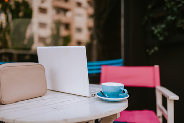 Pink pastel women's bag, laptop and cup of coffee on table in cafe