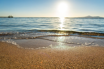 Close up of small sea waves with clear blue water over yellow sand beach at summer sunny shore. © bilanol