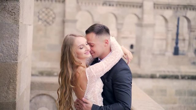 close up, portrait of attractive young couple hugging and kissing on nature against the backdrop of a refined castle room, central square of the old town, architecture. Blonde girl and man in black 