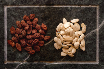 Top view of two almonds piles with blanched almonds and with peel on soapstone tray.