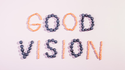 Vitamins and supplements for healthy eyes on pink background. How to maintain good vision concept. Blueberry and orange capsules forming words good vision, flat lay, top view