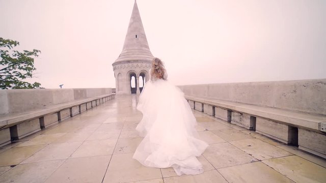 Fashion model, the bride in a chic wedding long dress running walks or walks, from behind and from the outside, looks around. against the background of the architecture of the old town and castle