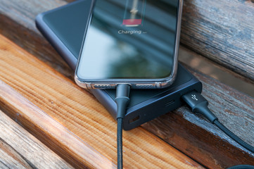 Modern smartphone charges from the power bank on the wooden background. Modern technology....