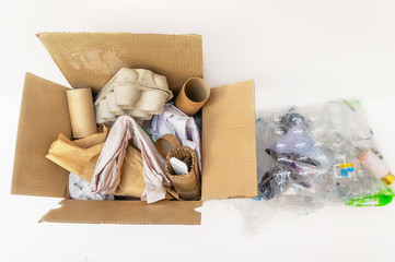 Sorting household waste at home. Cardboard, paper in box and plastic in a transparent bag on white background. The environment, separate waste collection, the concept of recycling.