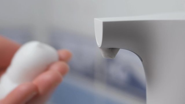 Women's hands use an automatic dispenser with liquid soap and wash under water.