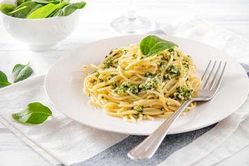 pasta with spinach and cheese on a plate, fork,  towel,  fresh spinach leaves on a light
