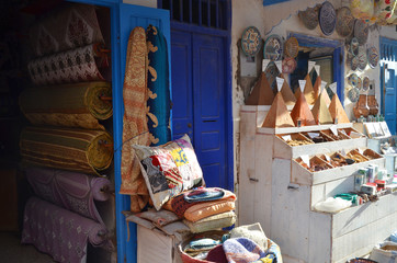 Moroccan counter with spices, ceramic dishes, souvenirs and carpet near a private, small shop.
