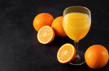 orange juice, fresh whole and half oranges on a black background, citrus drink
