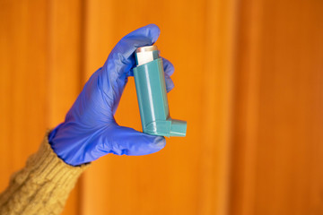 Gloved hands holding an asthma inhaler.