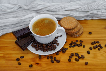 View of a white coffee cup full of black coffee surrounded by chocolate bars, coffee beans and cookies standing on wooden table