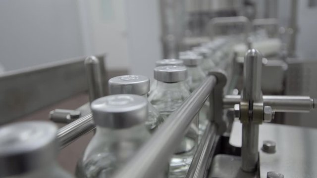 glass bottles filled and sealed with rubber and aluminum caps on medical solution conveyor line close up selective focus medical industry
