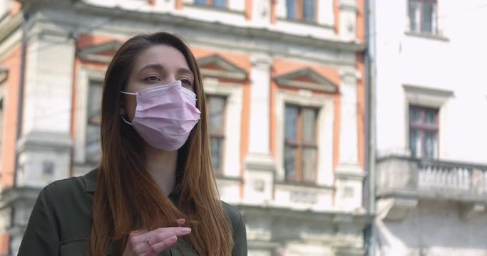 Young woman in pink protective medical mask walks down to the street. Thinking about safety life, N1H1 coronavirus, virus protection, pandemic.